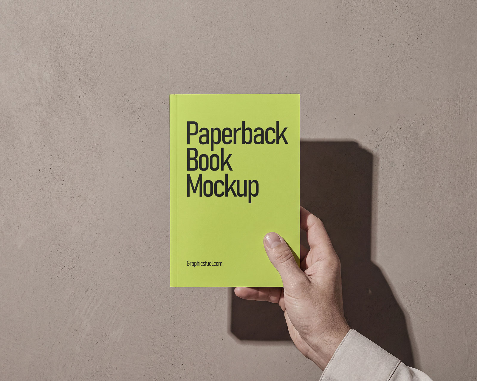 Free paperback book mockup held in hand against a warm plaster wall
