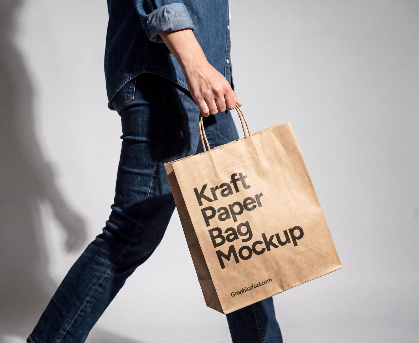 Hand holding a kraft paper bag mockup against a plain grey wall
