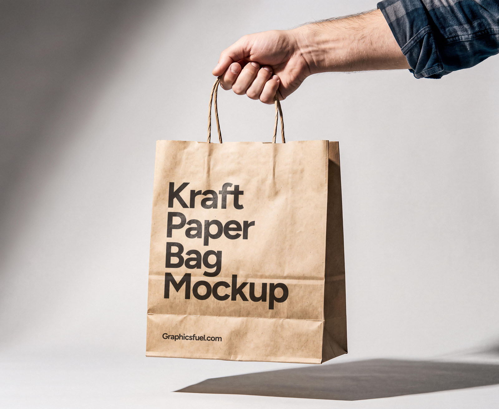 Hand holding a kraft paper bag mockup against a plain grey wall