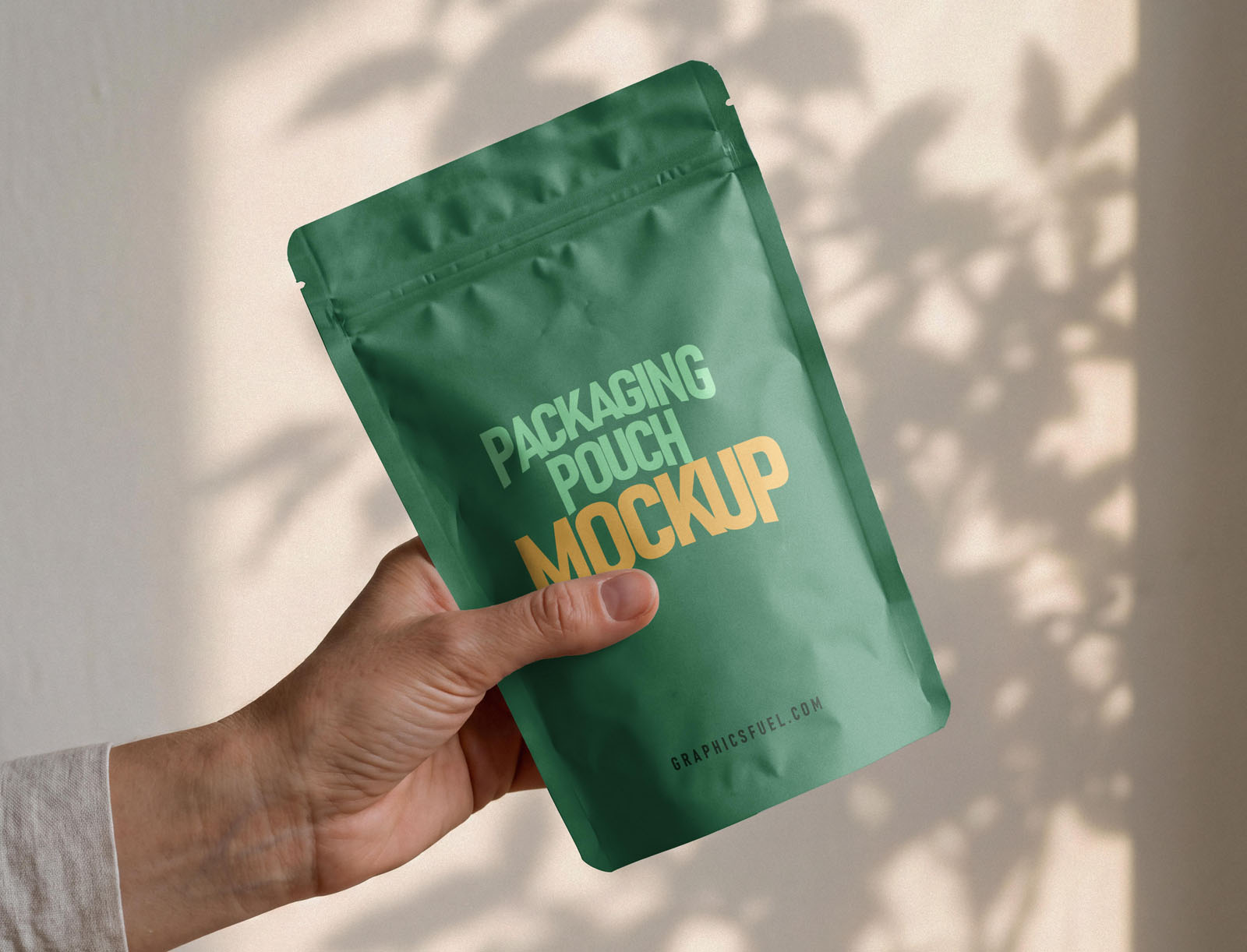 Green packaging pouch mockup held at an angle in natural light with foliage shadows