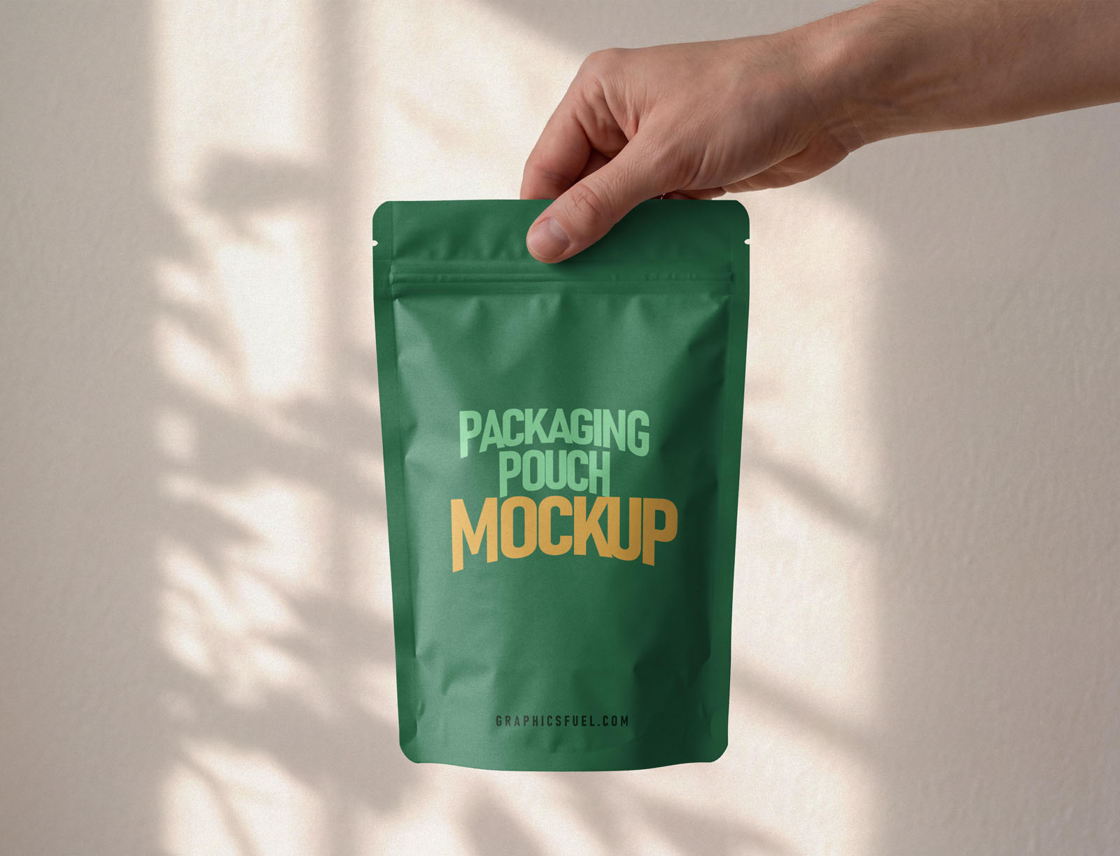 Hand gripping the top of a green stand-up pouch mockup against a warm wall