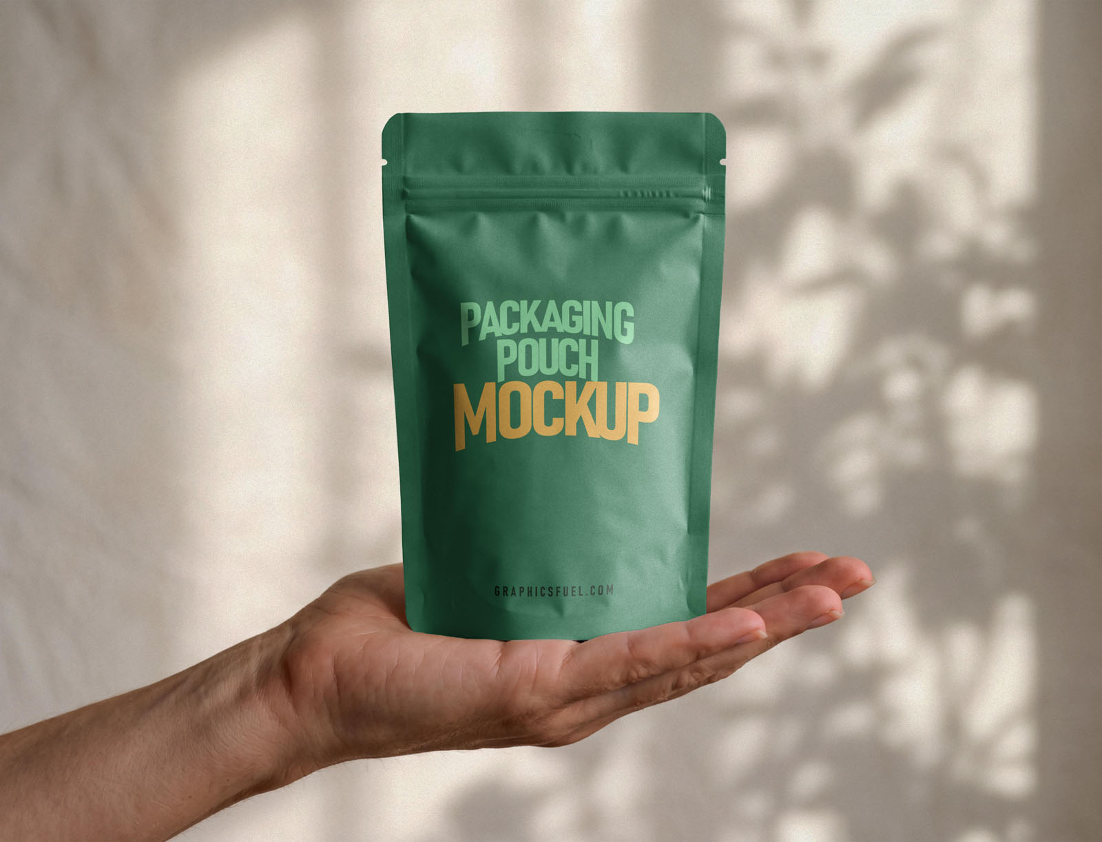 Hand gripping the top of a green stand-up pouch mockup against a warm wall