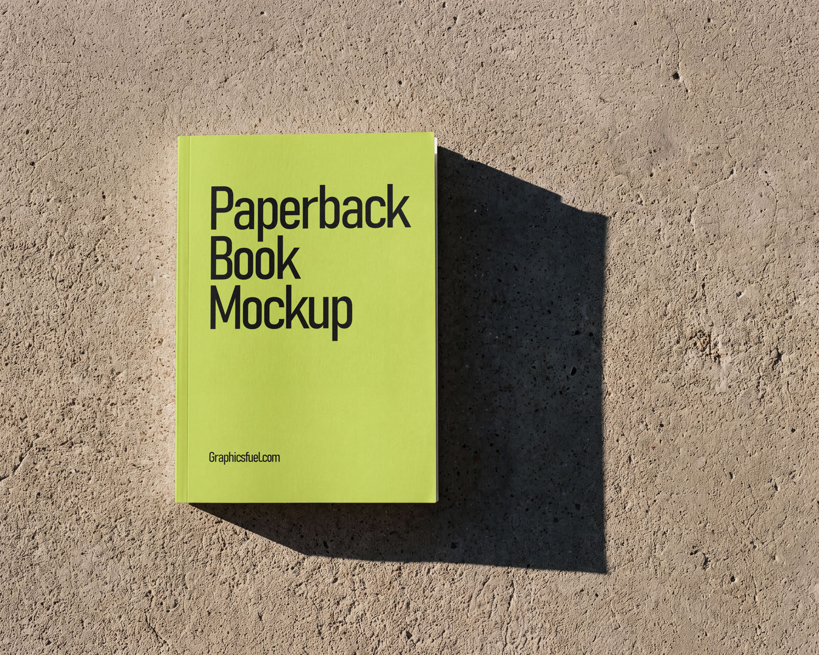 Paperback book mockup lying flat on rough concrete with a hard shadow